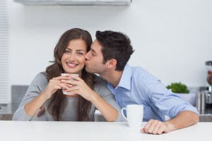 Man kissing wife while she smiles & holds coffee cup